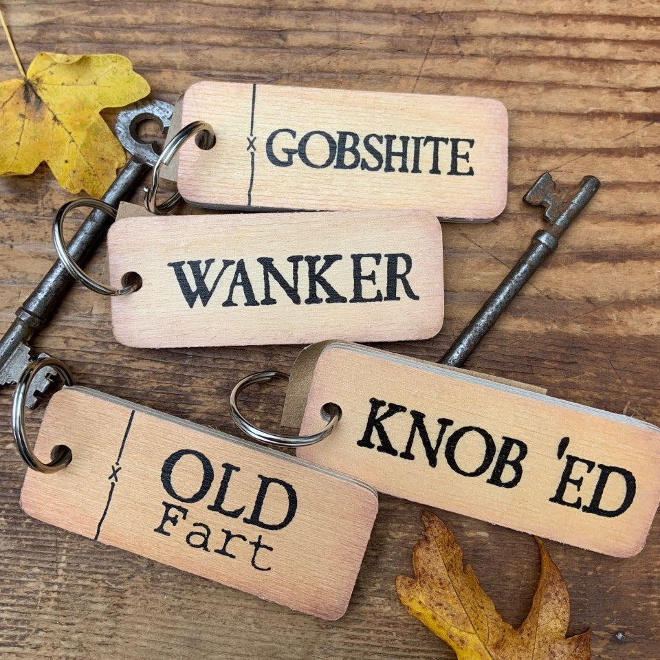 Wooden keychains with funny text on a wooden surface with keys and leaves.