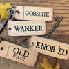 Wooden keychains with Funny sweary text on a wooden surface with keys and leaves.
